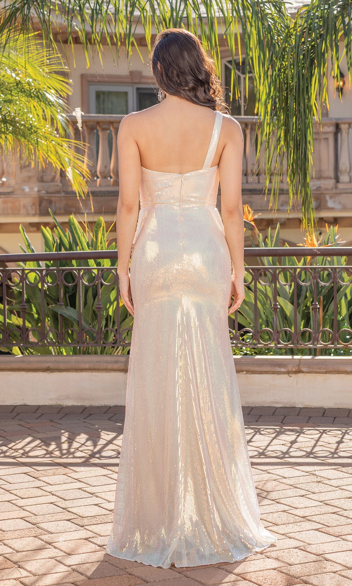 A woman stands outdoors with her back to the camera, wearing the One-Shoulder Long Shimmer Prom Dress with Slit. Her long, wavy hair flows down as she shows off the dress’s elegant, floor-length shimmer and modern one-shoulder design.